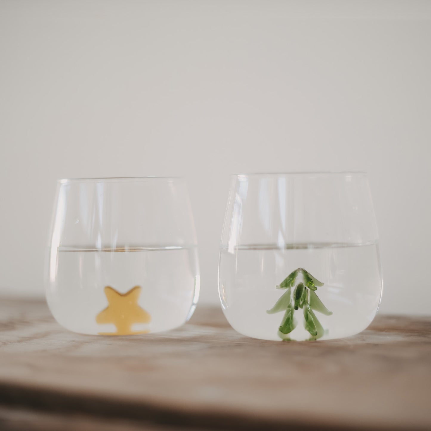 Zwei Trinkgläser Tannenfigur mit Wasser gefüllt, eines mit grünem Tannenbaum und eines mit gelbem Stern am Boden