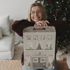 Frau lehnt lächelnd auf dem Eulenschnitt Signature-Adventskalender vor einem Weihnachtsbaum.