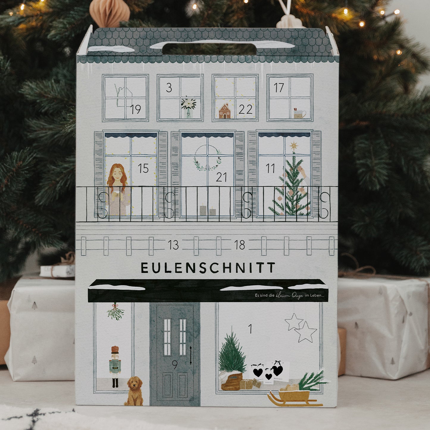 Eulenschnitt Adventskalender vor festlichem Weihnachtsbaum und Geschenken – liebevoll gestaltete Vorderseite.