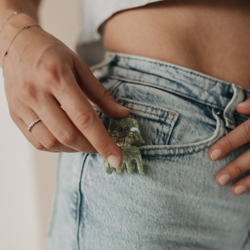 Hand greift nach der Haarspange klein Herz jade, die in der Gesäßtasche einer hellblauen Jeans steckt.