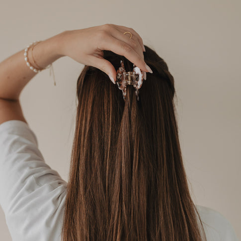 Hand greift nach Haarpartie mit großer Haarspange Herz Almond in halboffener Frisur von hinten.