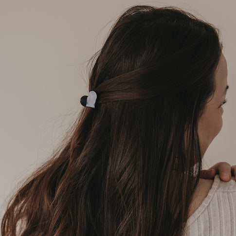 Kleine Haarspange in Herzform schwarz hält halboffenes braunes Haar seitlich zusammen