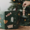 Eulenschnitt Adventskalender neben einem Weihnachtsbaum beim Aufhängen eines Baumanhängers