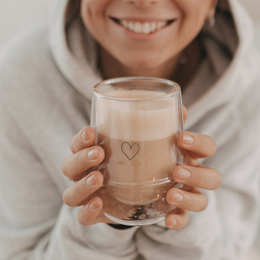 Lächelnde Frau hält ein doppelwandiges Cappuccino-Glas mit Herzmotiv in beiden Händen