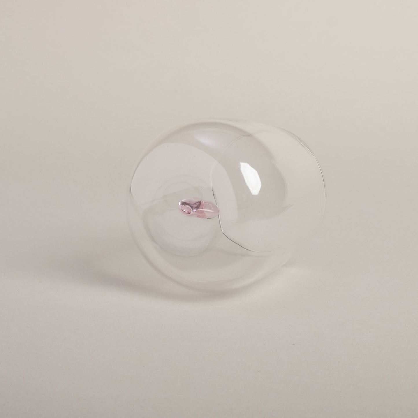 Klares Trinkglas mit rosa Herzfigur am Boden, schlichtes Design auf hellem Boden von unten fotografiert.