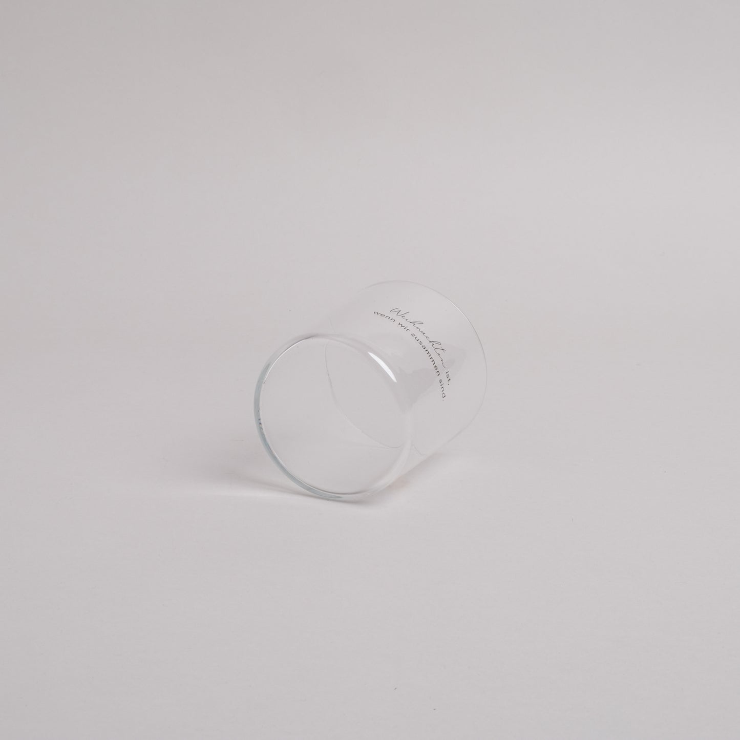 Trinkglas mit schwarzem Schriftzug „Weihnachten ist, wenn wir zusammen sind.“ – seitlich liegend fotografiert, schlichtes Weihnachtsdesign.