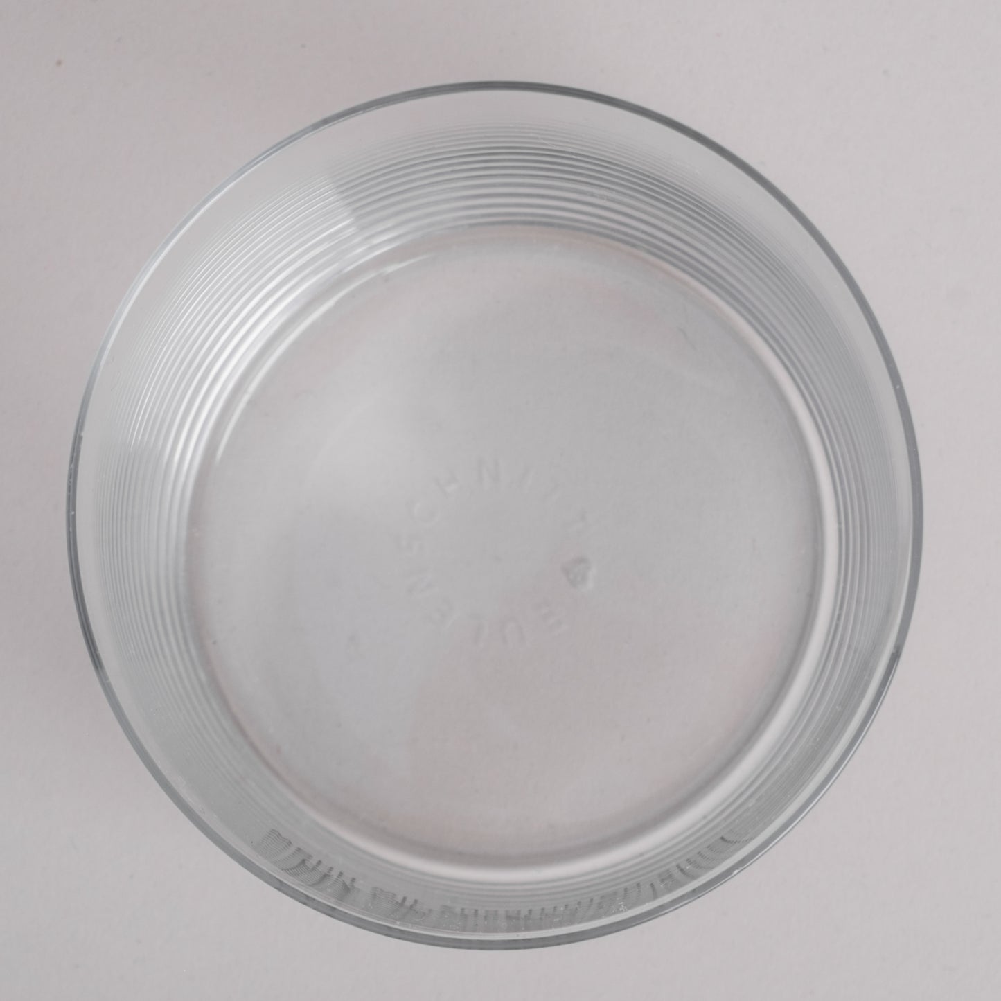 Draufsicht auf ein klares Trinkglas, geprägtem Eulenschnitt-Schriftzug am Glasboden 