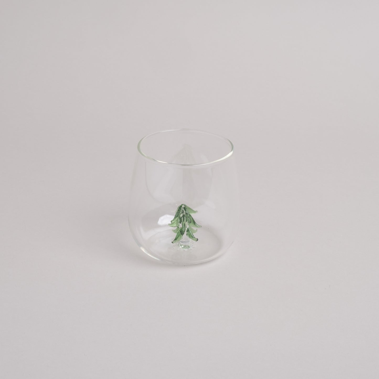 Klares Trinkglas mit grüner Tannenfigur als dekorativem Element im Glasboden