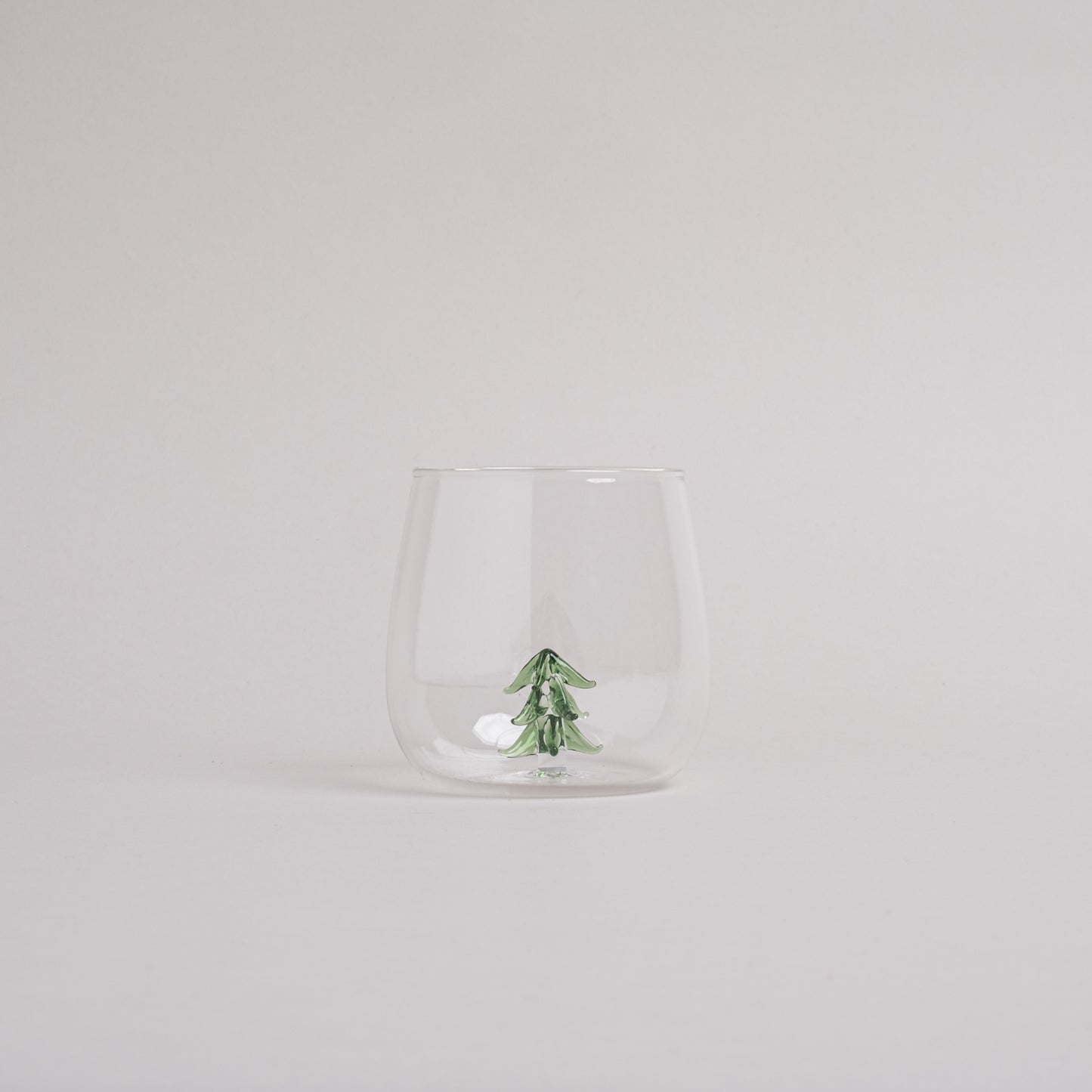 Trinkglas mit integrierter grüner Tannenfigur im Glasboden, modernes Design
