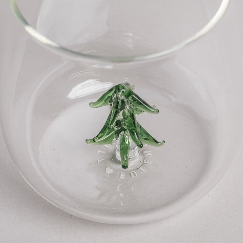 Trinkglas mit grüner Tannenfigur aus Glas im Boden, rund und transparent