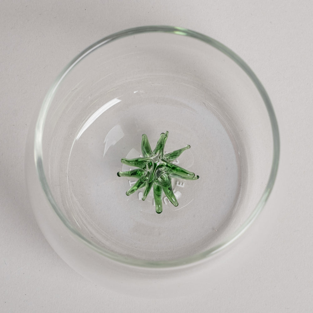 Trinkglas mit grüner Tannenfigur als dekorativem Element am Glasboden