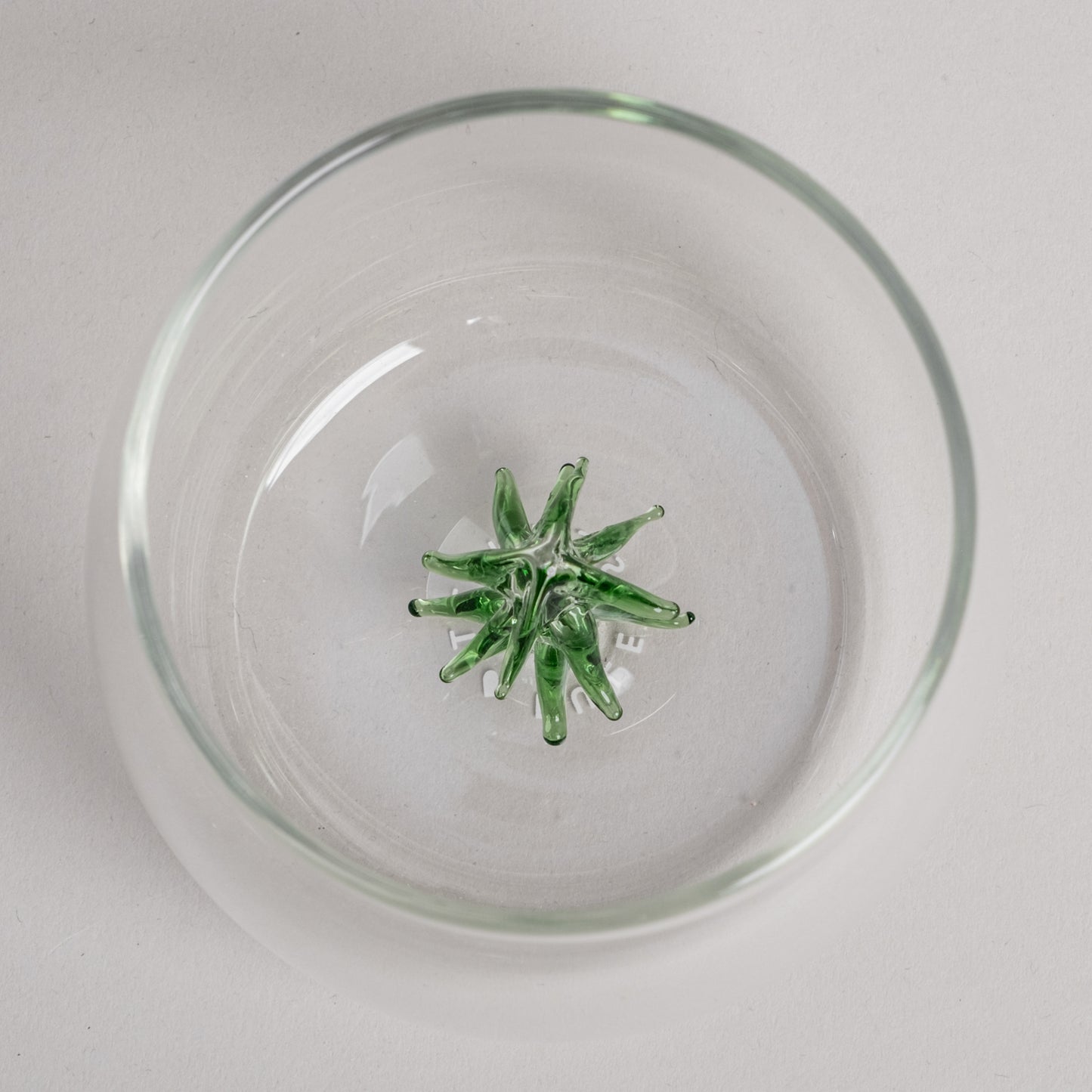 Trinkglas mit grüner Tannenfigur als dekorativem Element am Glasboden