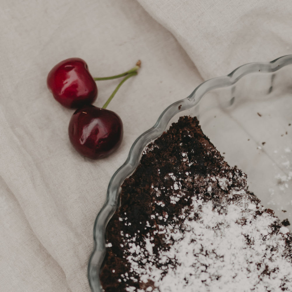 Nahaufnahme der angebrochenen Tarte mit zwei frischen Kirschen daneben