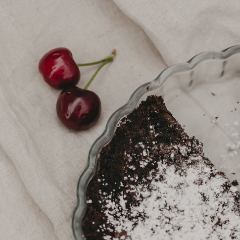 Nahaufnahme der angebrochenen Tarte mit zwei frischen Kirschen daneben