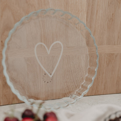 Tarteform mit weißem Herz auf Holzplatte dekorativ präsentiert, vorn Kirschen