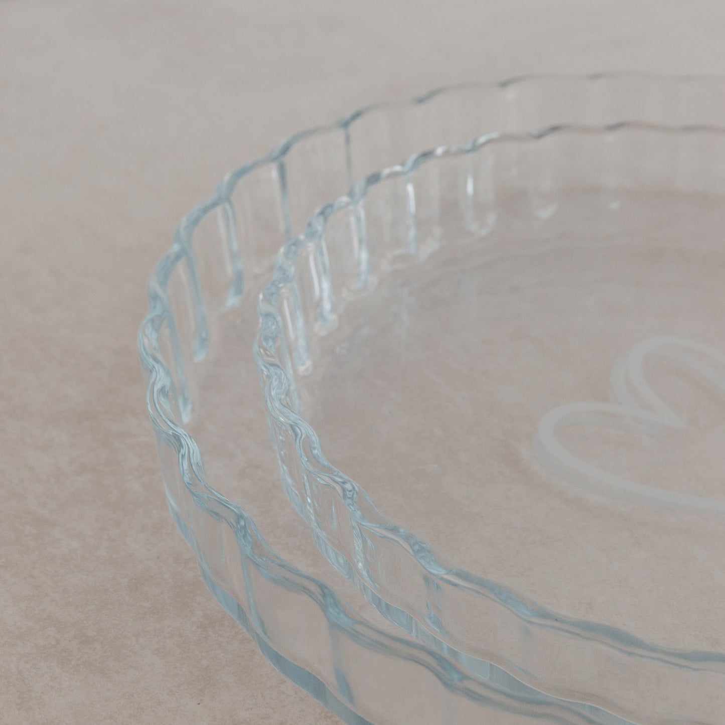 Nahaufnahme zweier gläserner Tarteformen mit gewelltem Rand und Herzgravur im Boden.