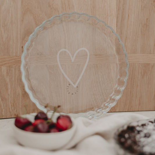 Kleine Tarteform Herz aus Glas stehend vor Holz, im Vordergrund Kirschen