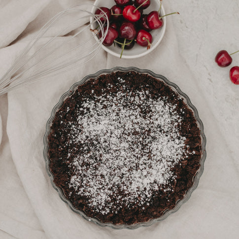 Schokoladentarte in Glasform mit Puderzucker bestäubt und Kirschen daneben