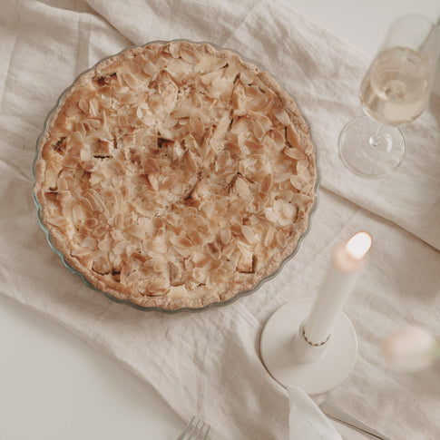 Frisch gebackene Tarte mit Mandelblättchen in großer Herz-Tarteform aus Glas auf festlich gedecktem Tisch.