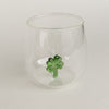 Figurglas mit grünem Kleeblatt im Inneren, transparentes Glas mit kleeblattförmiger Figur auf hellem Hintergrund fotografiert.