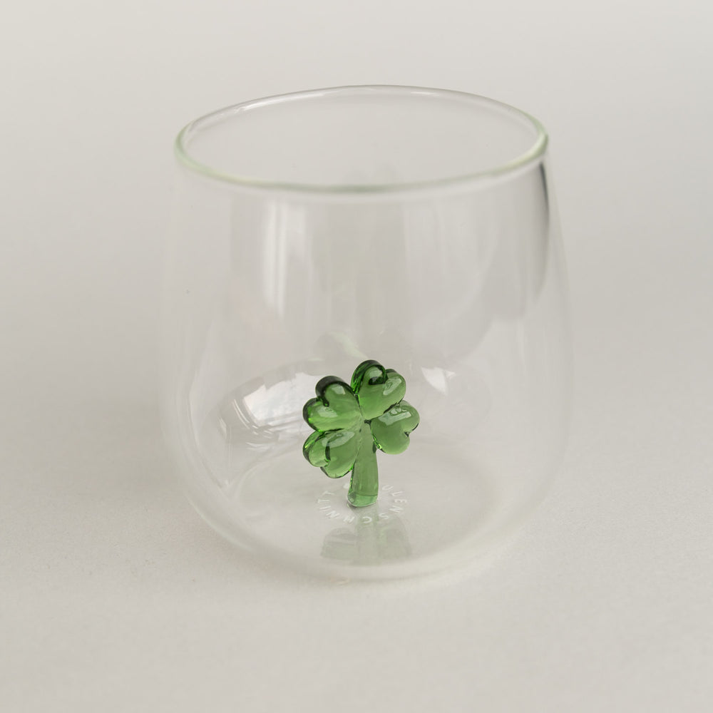 Figurglas mit grünem Kleeblatt im Inneren, transparentes Glas mit kleeblattförmiger Figur auf hellem Hintergrund fotografiert.
