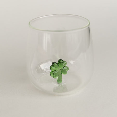 Figurglas mit grünem Kleeblatt im Inneren, transparentes Glas mit kleeblattförmiger Figur auf hellem Hintergrund fotografiert.