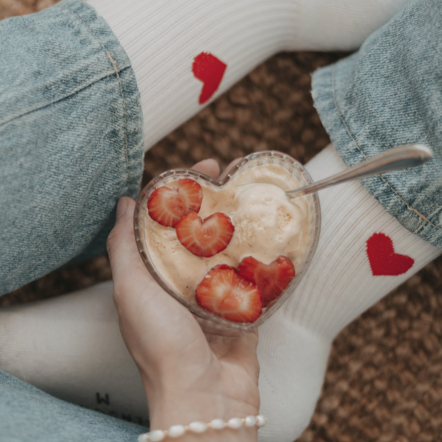 Herzförmige Glasschale mit Eis und Erdbeeren, serviert auf gemütlichem Setting mit Herzsocken.