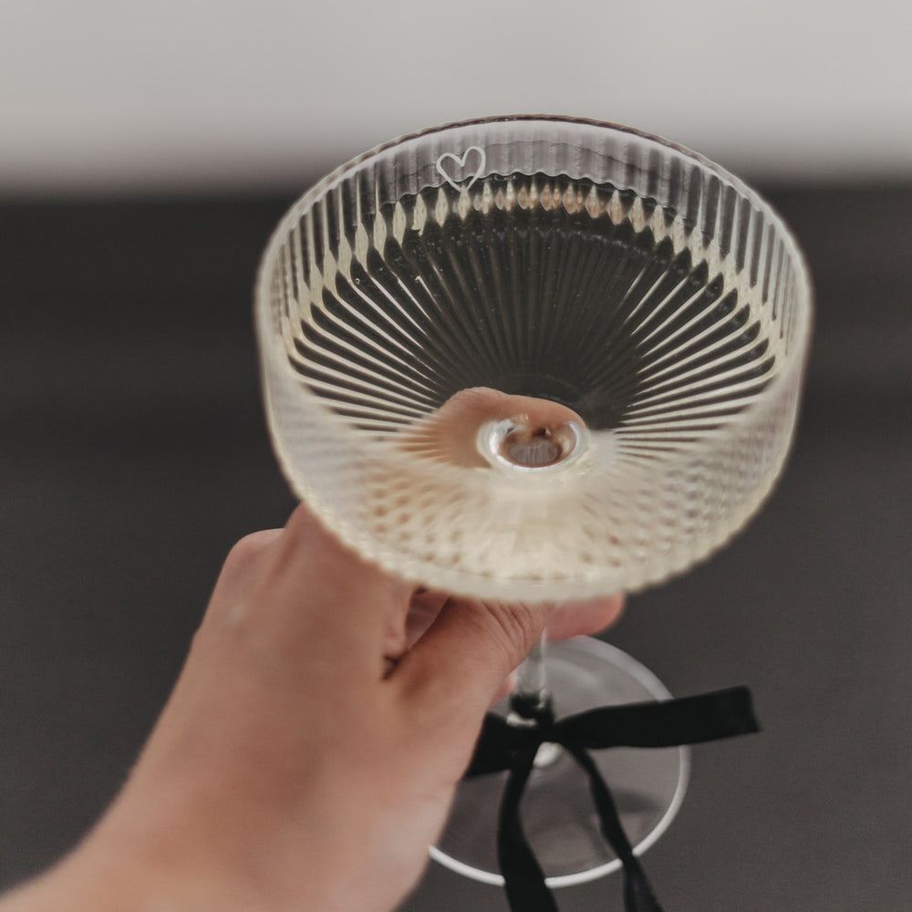 Hand hält gefülltes Champagnerglas mit feiner Riffelstruktur und Herzgravur am Rand.