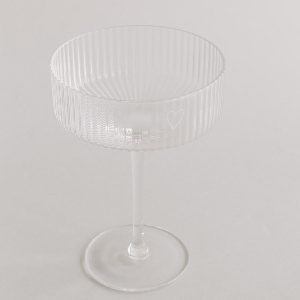 Einzelnes Champagnerglas mit Herzgravur auf hellem Hintergrund freigestellt.