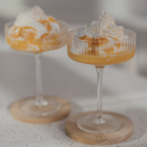 Nahaufnahme zweier Champagnergläser mit cremigem Dessert und Sahnehaube auf Holzuntersetzern.