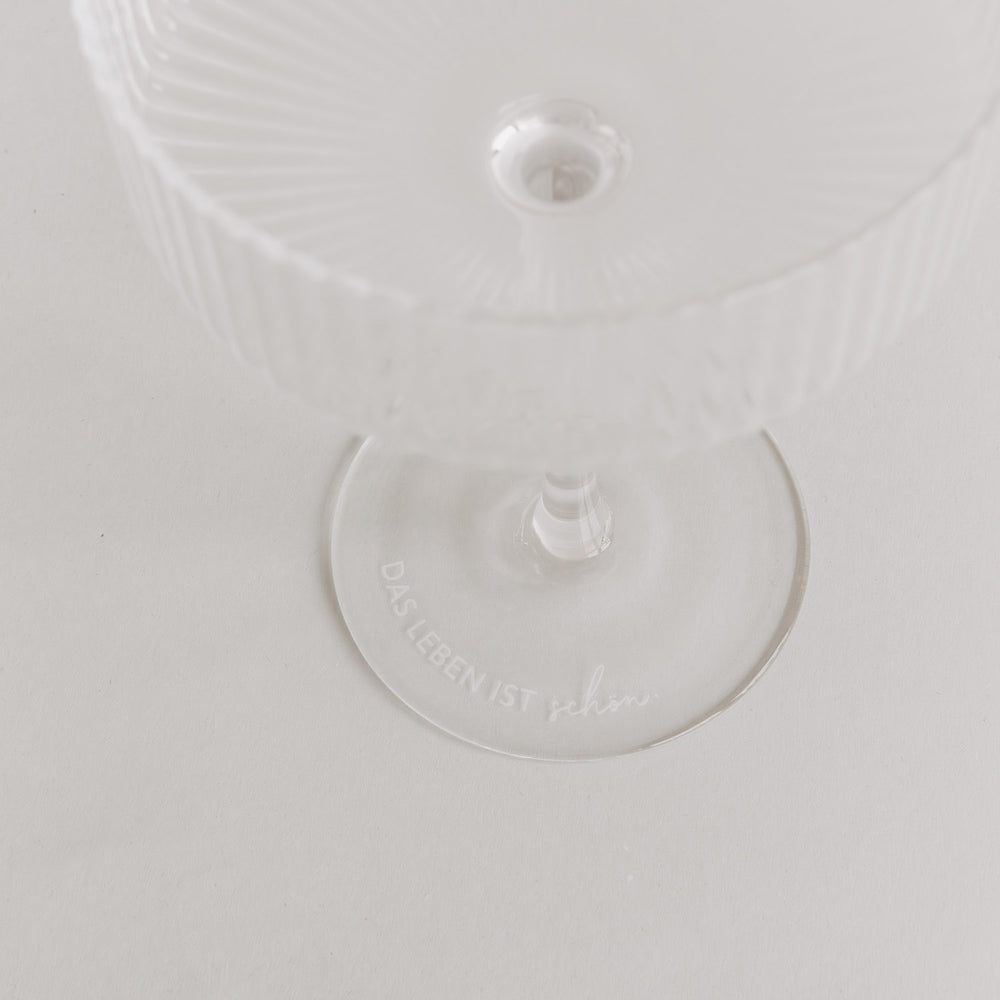 Minimalistisches Produktfoto: Glas mit Gravur „Das Leben ist schön“ auf weißem Untergrund.