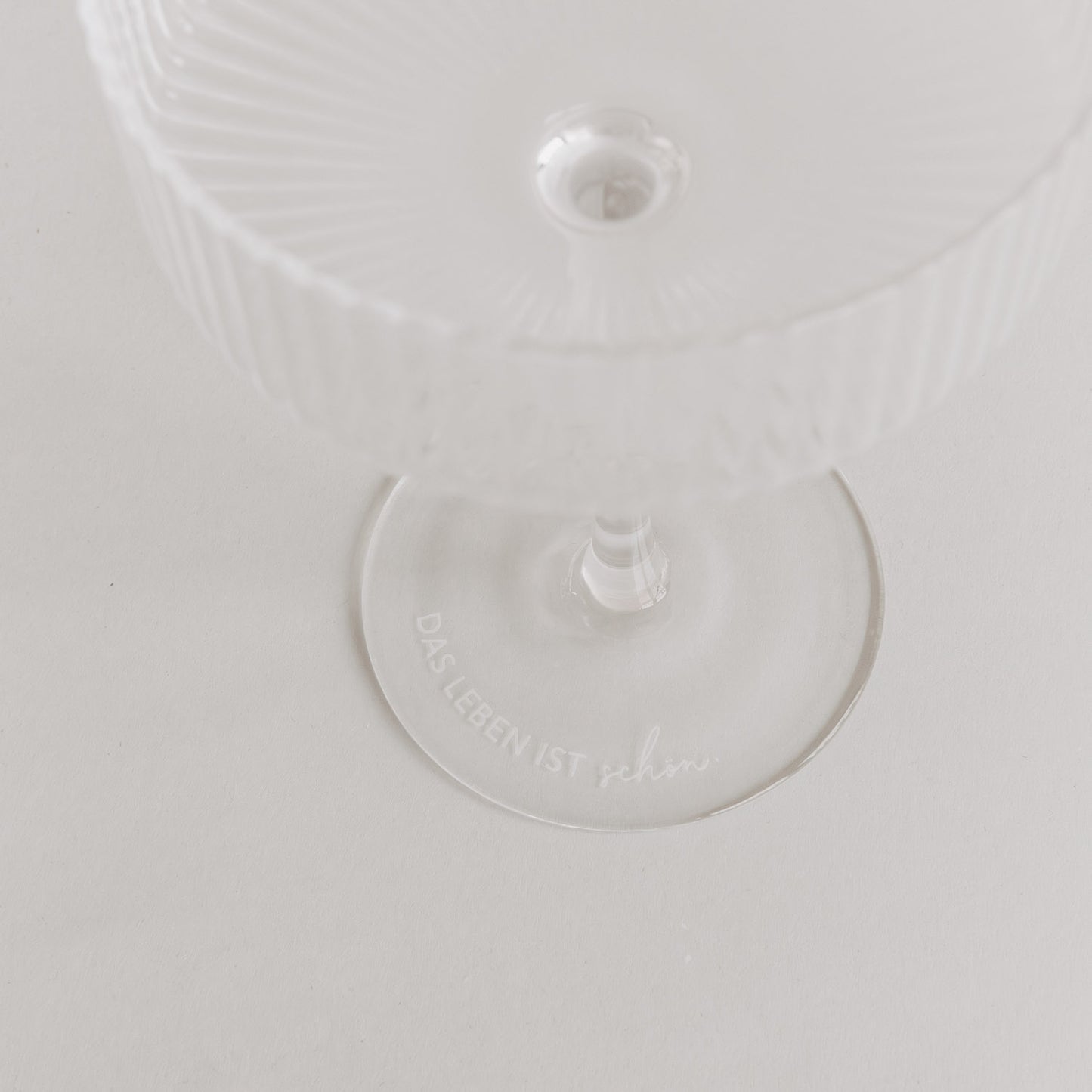 Minimalistisches Produktfoto: Glas mit Gravur „Das Leben ist schön“ auf weißem Untergrund.