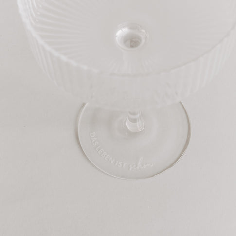 Minimalistisches Produktfoto: Glas mit Gravur „Das Leben ist schön“ auf weißem Untergrund.