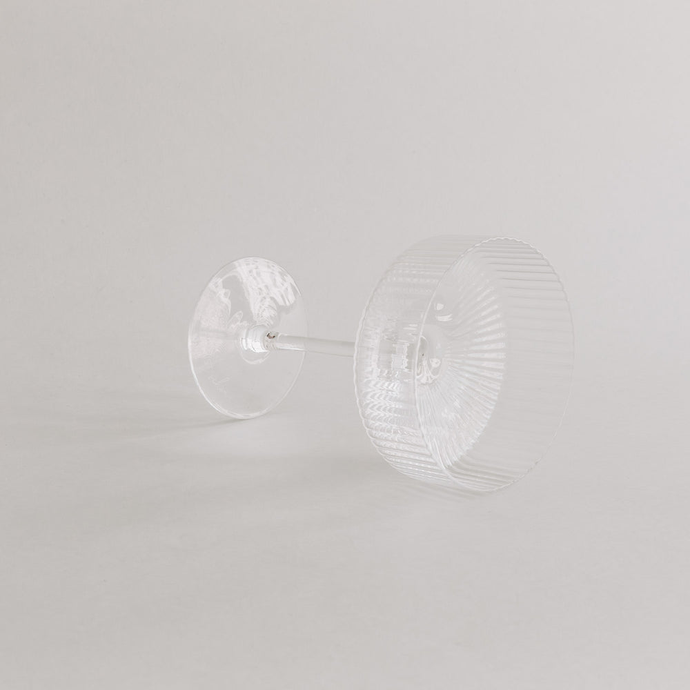 Champagnerglas liegt auf der Seite – Fokus auf Boden und Formgebung, vor hellem Hintergrund.