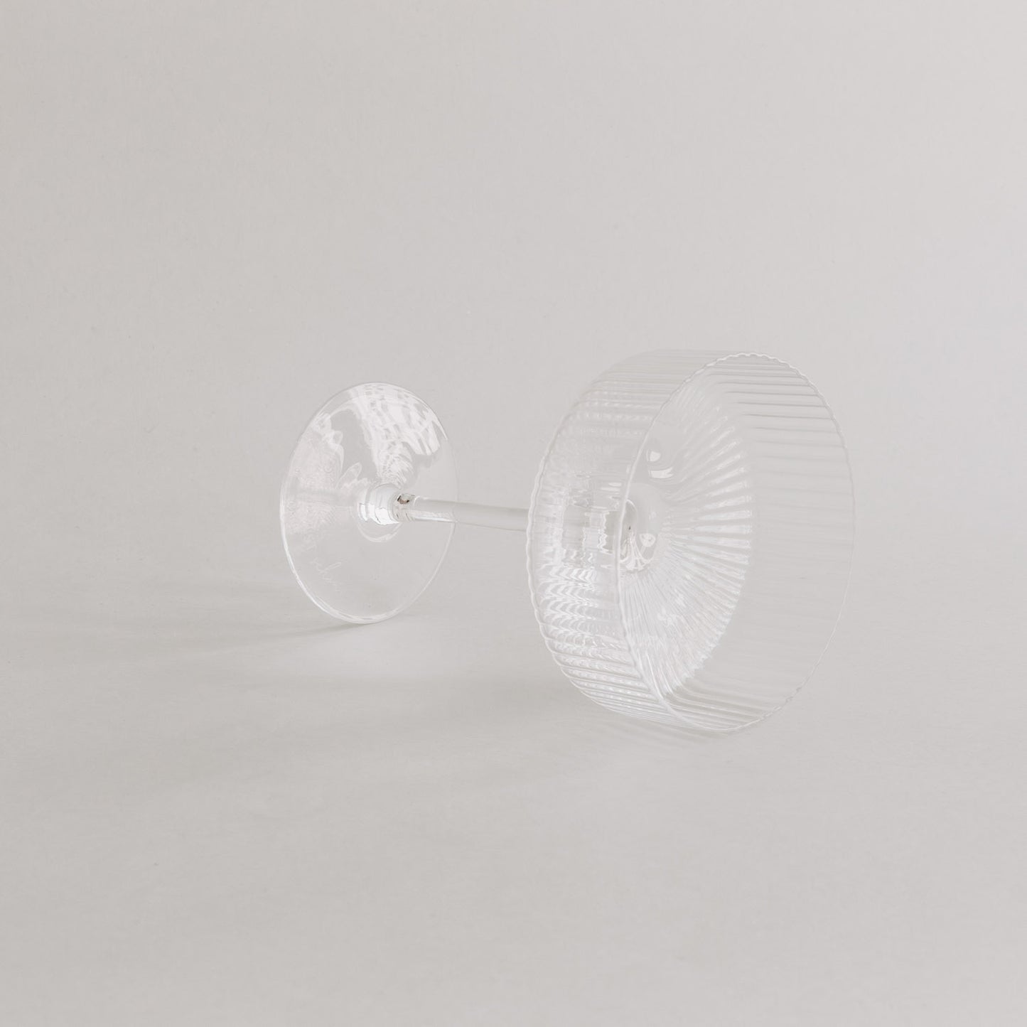 Champagnerglas liegt auf der Seite – Fokus auf Boden und Formgebung, vor hellem Hintergrund.