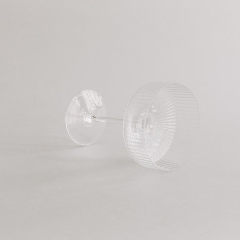 Champagnerglas liegt auf der Seite – Fokus auf Boden und Formgebung, vor hellem Hintergrund.