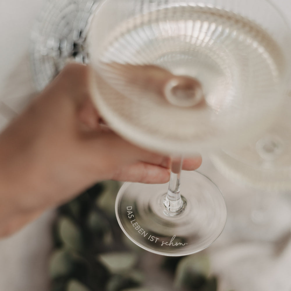 Nahaufnahme des Glasfußes mit Gravur „Das Leben ist schön“ in eleganter Schrift.