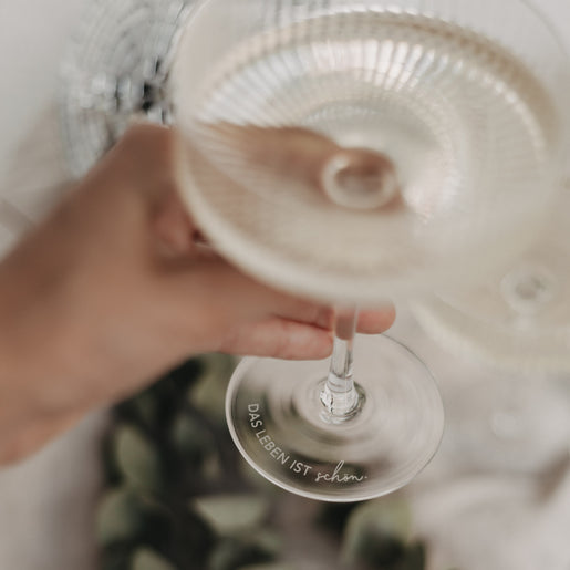 Nahaufnahme des Glasfußes mit Gravur „Das Leben ist schön“ in eleganter Schrift.