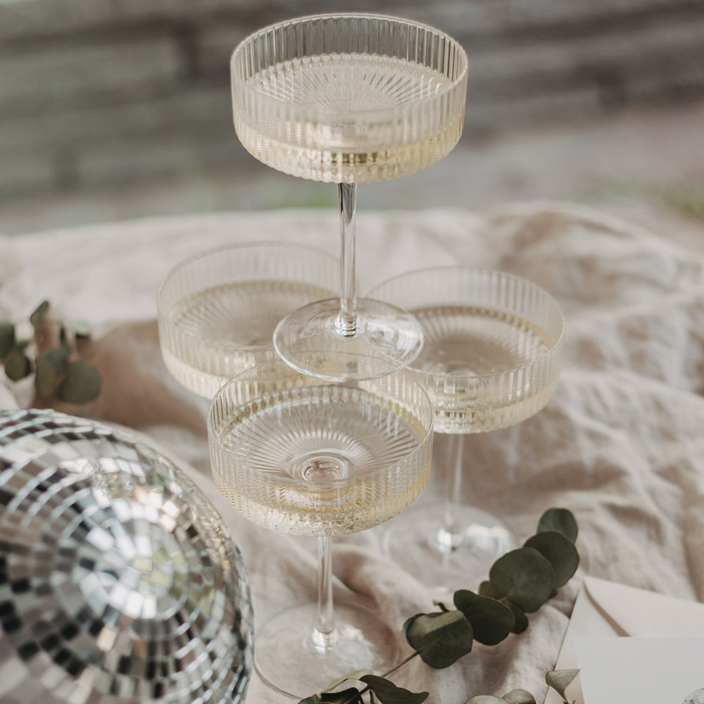 Vier gefüllte Champagnergläser in Pyramidenanordnung – stimmungsvolles Arrangement mit Diskokugel.