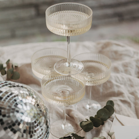 Vier gefüllte Champagnergläser in Pyramidenanordnung – stimmungsvolles Arrangement mit Diskokugel.