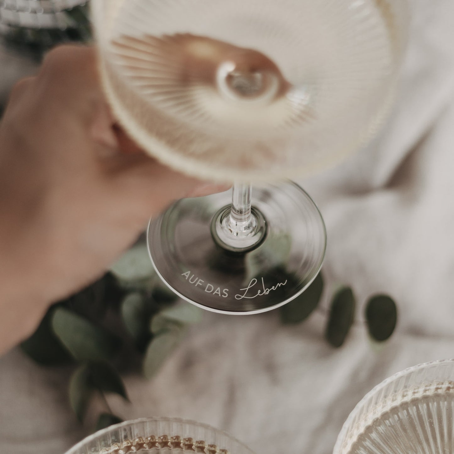 Gravur „Auf das Leben“ am Boden eines gefüllten Champagnerglases, stilvoll serviert.