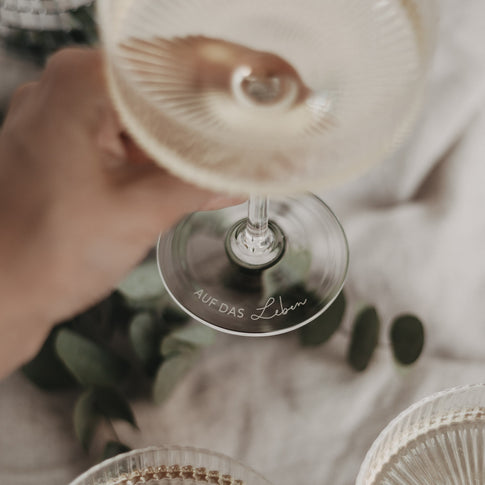 Gravur „Auf das Leben“ am Boden eines gefüllten Champagnerglases, stilvoll serviert.