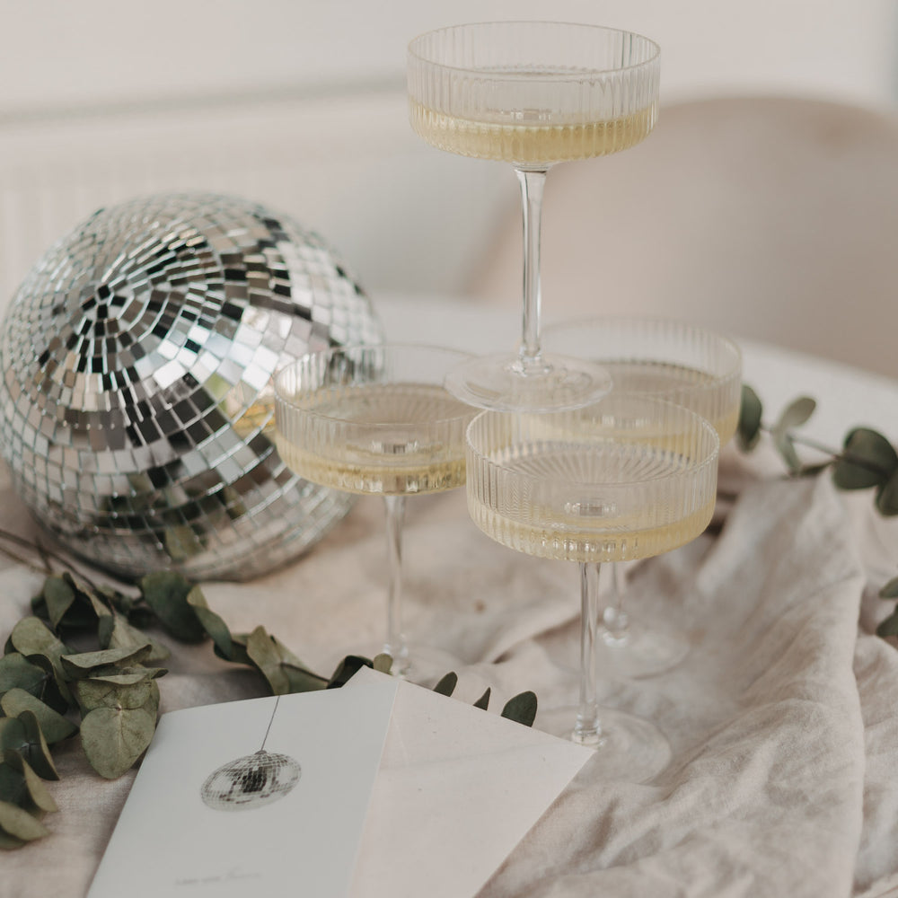 Vier gestapelte Champagnergläser mit Disco-Kugel und Eukalyptus, festlich arrangiert.