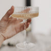 Hand hält elegantes Champagnerglas mit feinem Rillendesign, goldener Drink im Glas.