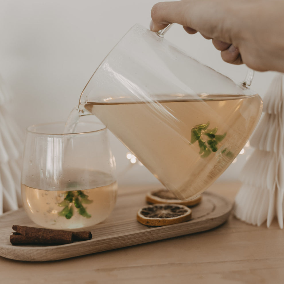 Hand gießt Getränk aus der Karaffe mit grünem Tannenbaum – stilvoll servieren mit winterlichem Flair.