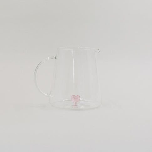 Karaffe aus Glas mit rosa Herzfigur im Inneren, minimalistisch vor weißem Hintergrund inszeniert.