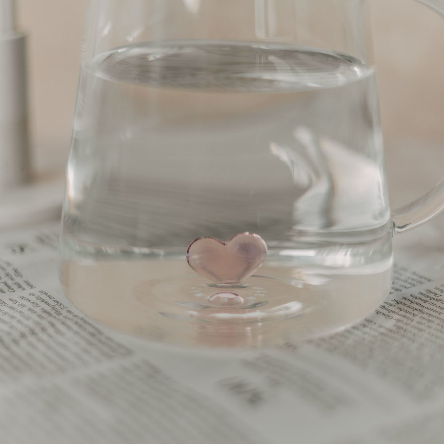 Seitlicher Blick durch klares Wasser auf die rosa Herzfigur im Inneren der Karaffe.