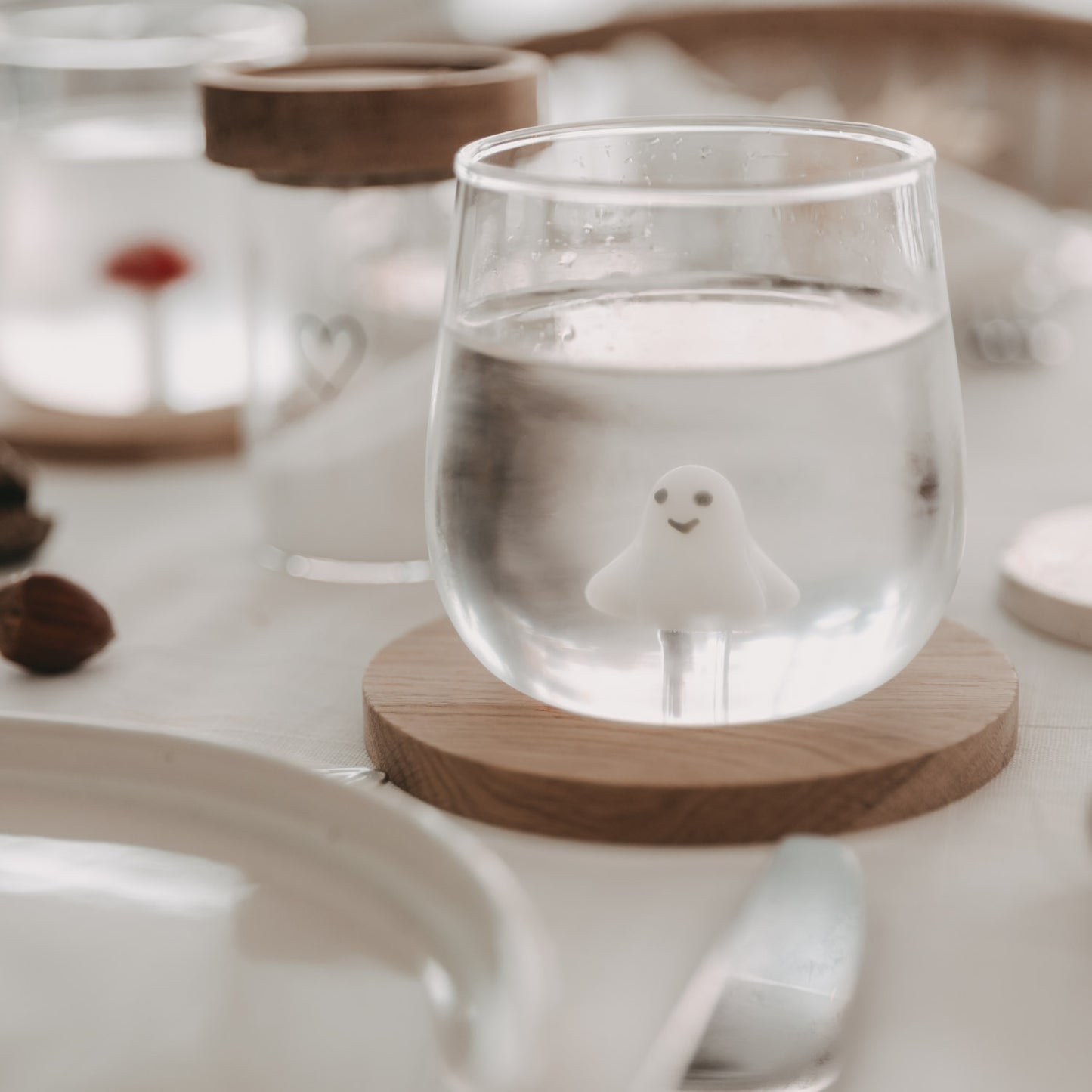 Trinkglas mit 3D-Geistfigur auf gedecktem Tisch, stilvoll dekoriert mit Holzuntersetzer und Vorratsglas