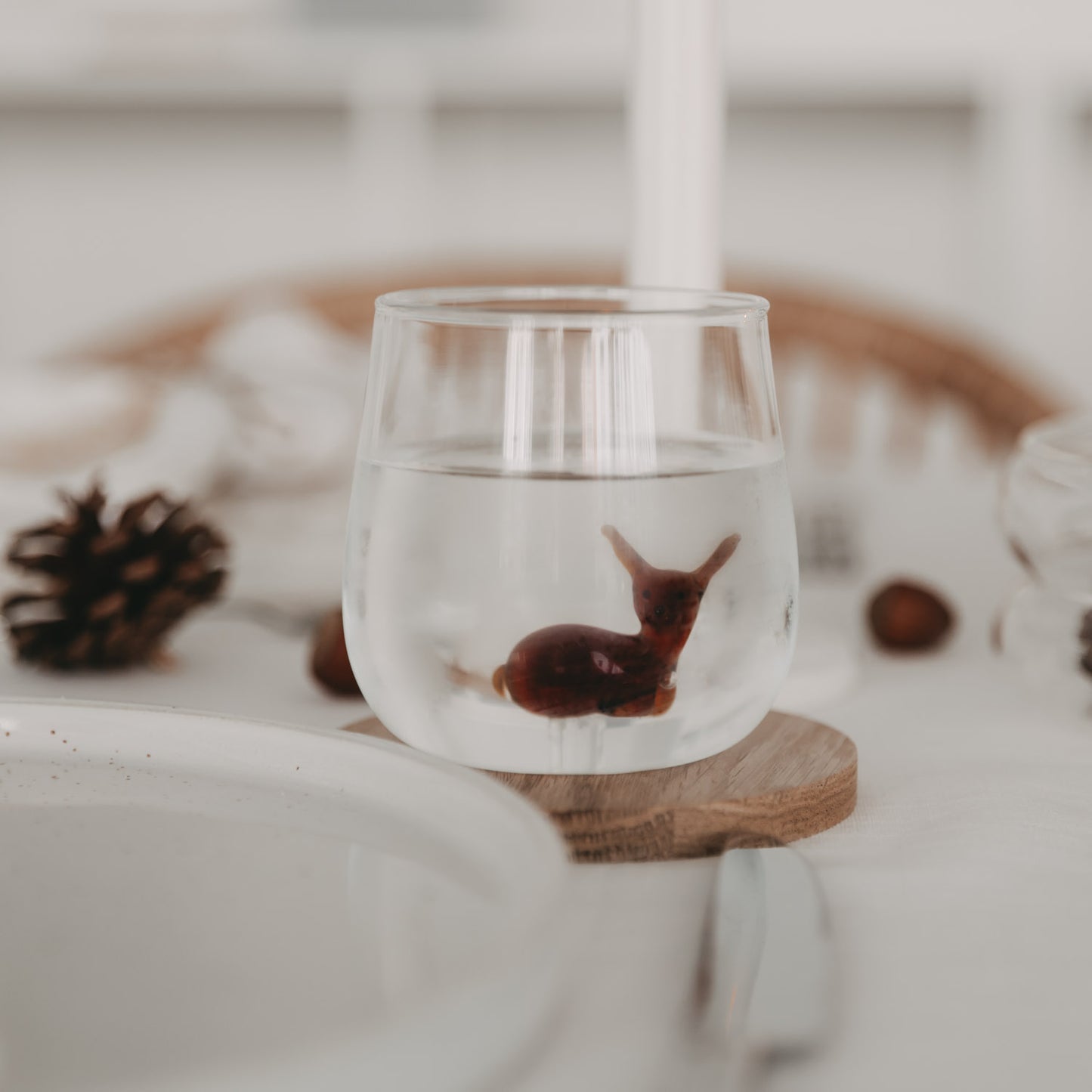 Rehfigur scheinbar schwebend im gefüllten Glas mit Wasser – ein bezaubernder Moment am gedeckten Tisch.