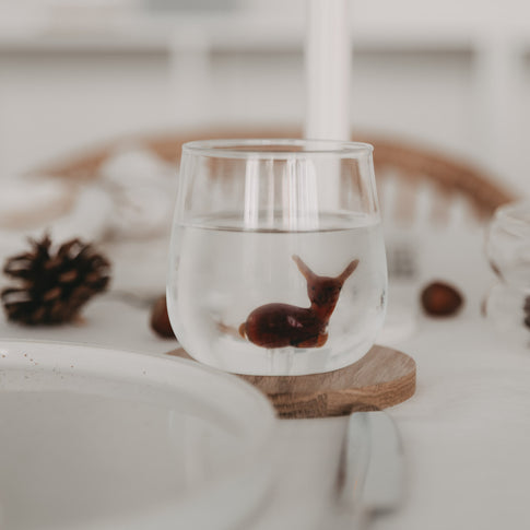 Rehfigur scheinbar schwebend im gefüllten Glas mit Wasser – ein bezaubernder Moment am gedeckten Tisch.